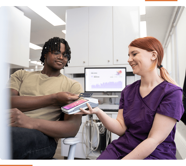 Person paying with a phone on a card reader held by a smiling dental professional in a clinic.