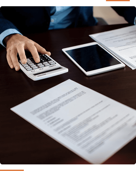A person using a calculator at a desk with documents and a tablet.