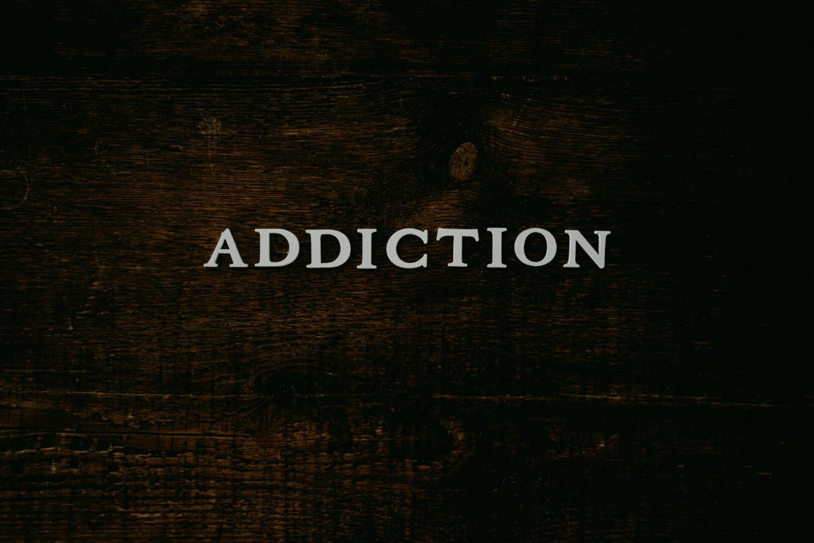 The word "ADDICTION" in white capital letters on a dark, textured wooden background.