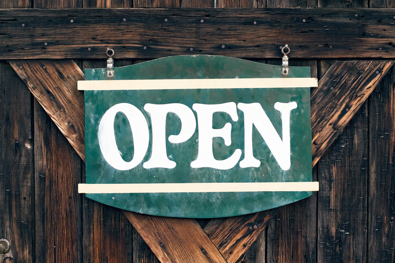 3 A green sign with the word "OPEN" in white capital letters hangs on a rustic wooden door.
