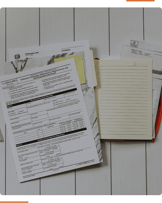 A stack of papers including tax-related documents, a notebook, and a red pen on a wooden surface.