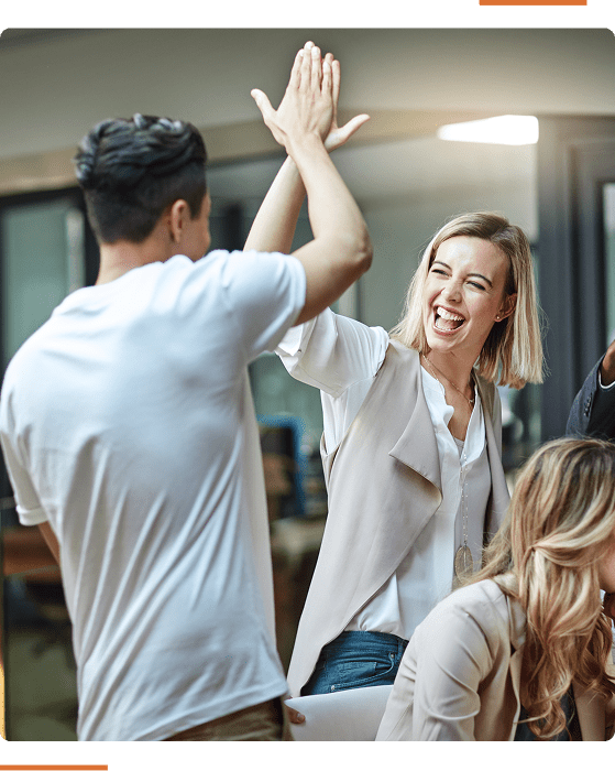 Group 304 (1) Two individuals in an office setting exchange a high-five. The woman smiles broadly while seated, and the man stands with his back turned.