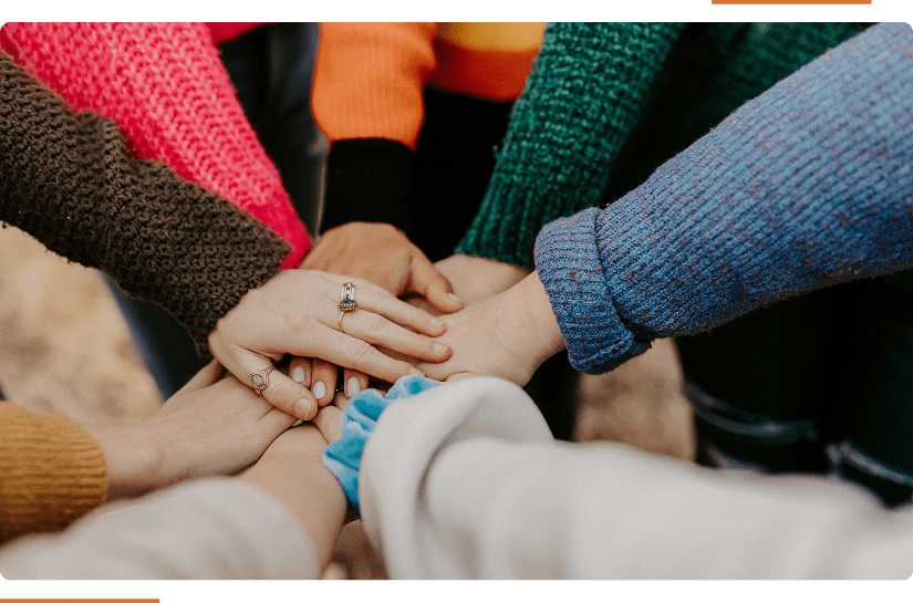 A group of people placing their hands together in the center, wearing colorful sweaters.