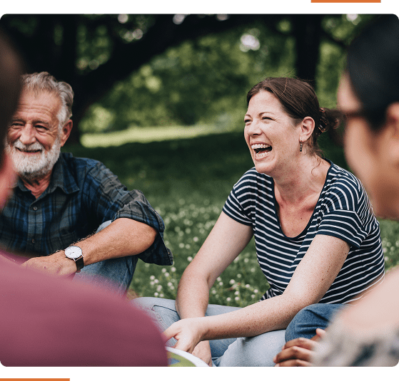 Group of people sitting on grass, smiling and chatting in a park setting.
