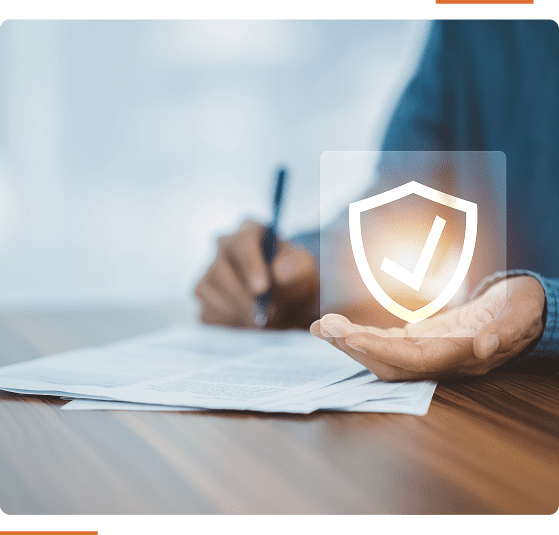 Person signing documents, with a digital shield and checkmark icon floating above their other hand, symbolizing protection or authorization.